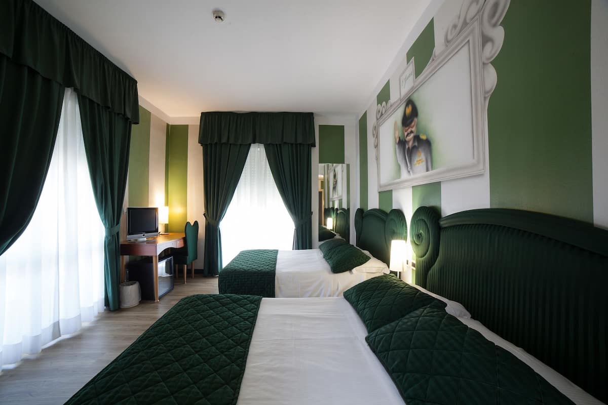 A hotel room with two beds, a desk, a chair, and a television.