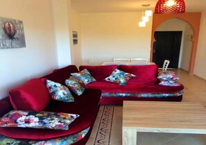 Um sofá vermelho com almofadas florais, uma mesa de centro de madeira e um chão de azulejos.