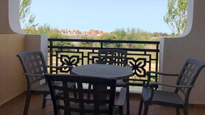 Un balcón con mesa y sillas, baranda de metal decorativa y vistas a edificios en la distancia.