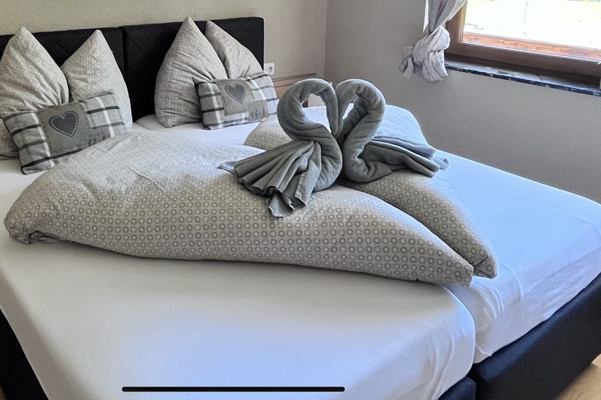 A neatly made bed with pillows and a towel arranged in a heart shape.