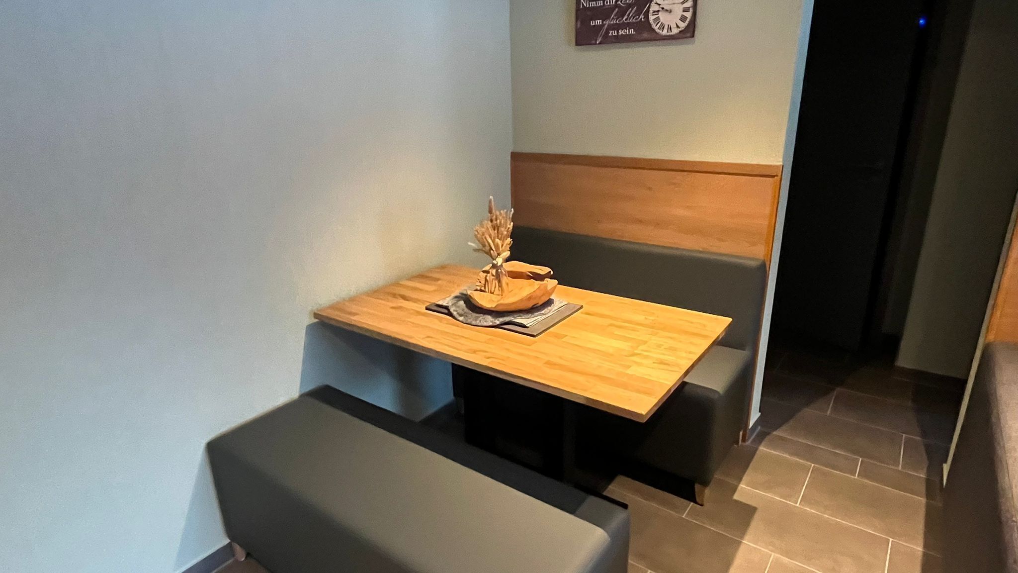 Un espacio comedor pequeño y privado con una mesa de madera y un banco, un jarrón decorativo y un reloj en la pared.