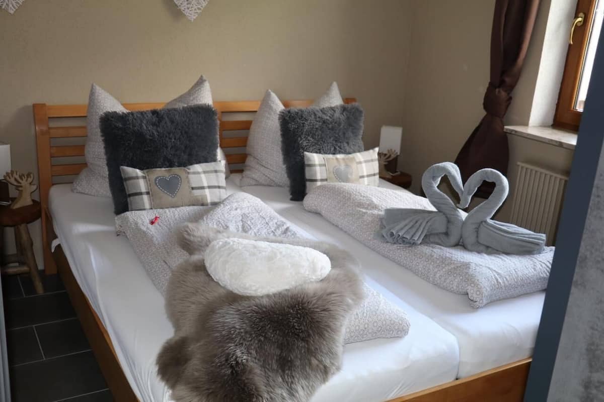 A neatly made bed with pillows, a fluffy rug, and towels arranged in a swan shape.