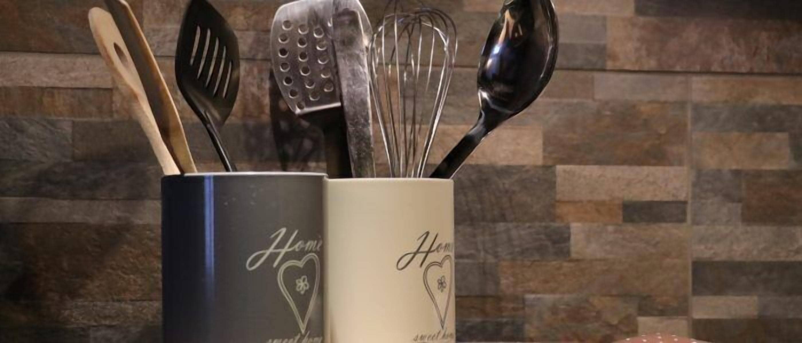 A kitchen utensil holder with two mugs, one black and one beige, both labeled "Home sweet home."