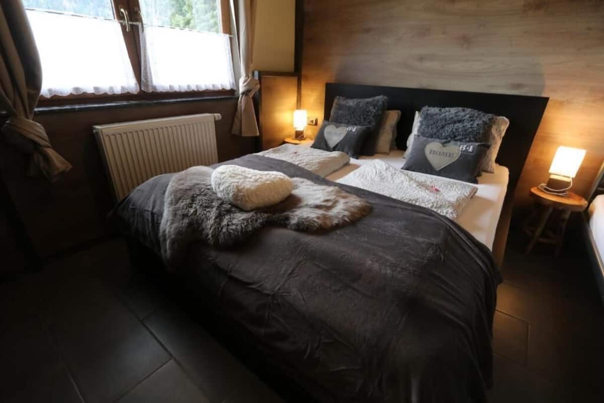A bedroom with a large bed, two bedside lamps, a radiator, and a window with curtains.