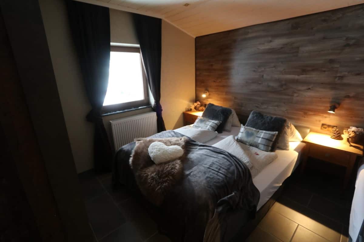 A bedroom with a bed, a nightstand, a lamp, and a window.