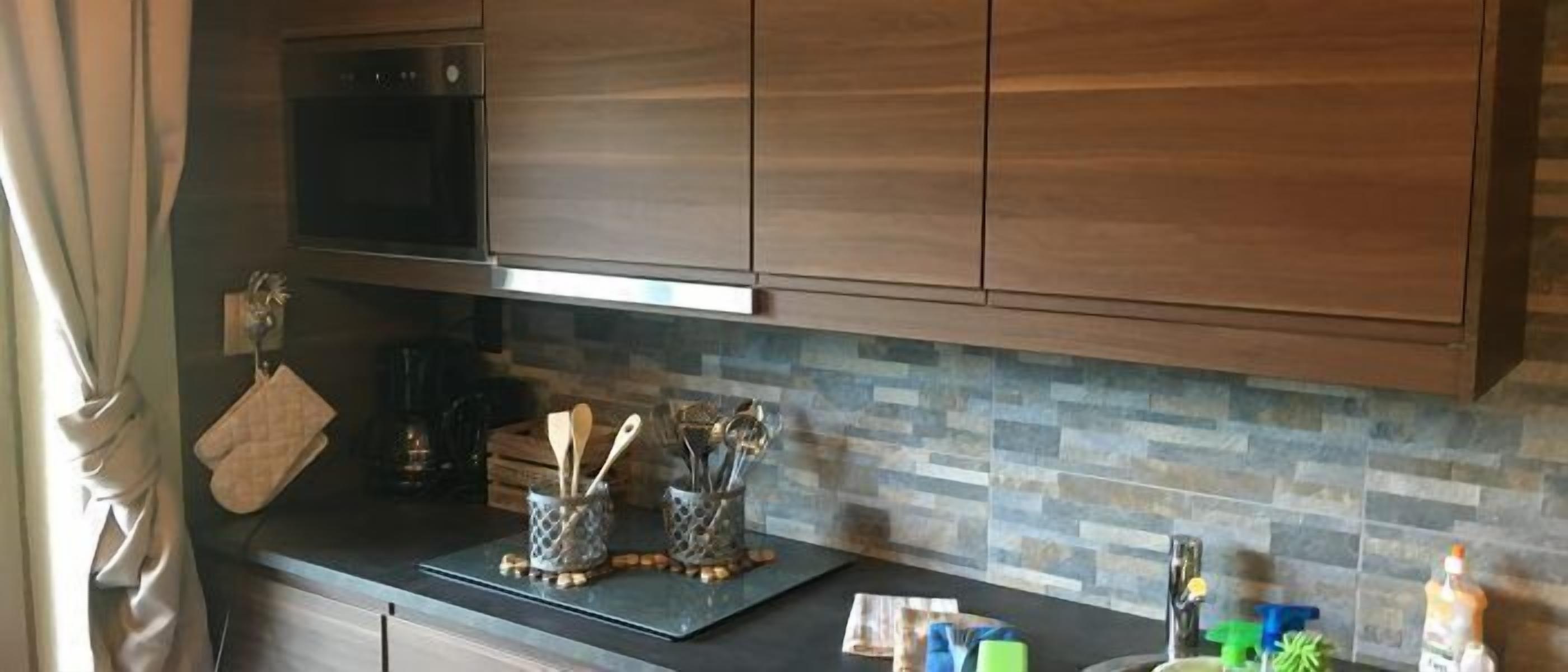A kitchen with wooden cabinets, a black oven, a tiled backsplash, and a countertop with utensils and a bottle.