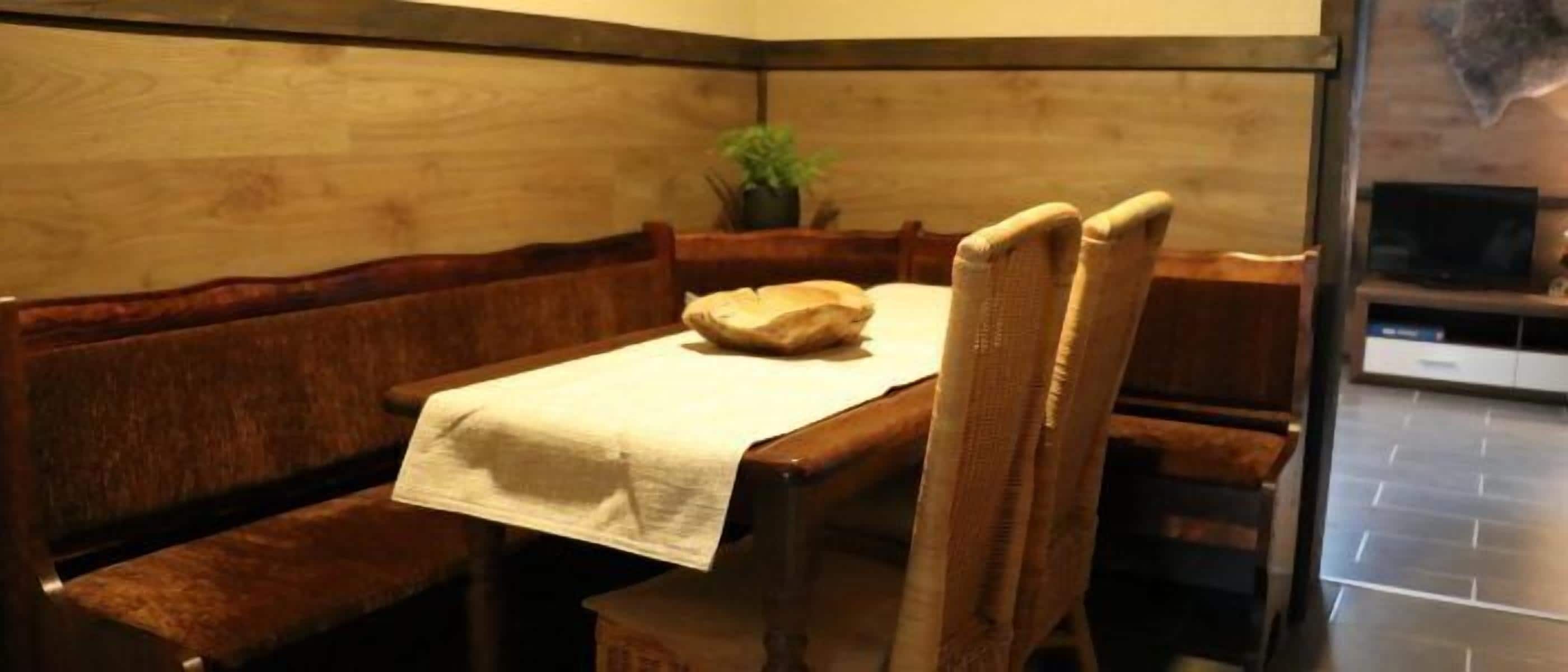 A dining area with a wooden table and chairs, a white tablecloth, and a potted plant.