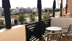 A balcony with a table and chairs, overlooking a residential area with buildings and a road. - Residence Marina Saidia 4244 (Saidia)