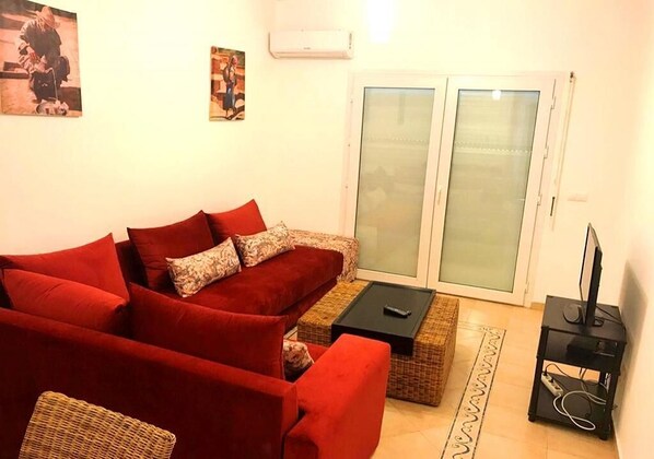 A living room with a red sofa, a black coffee table, and a television on a stand.