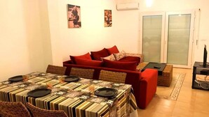 A dining area with a table set for four, a red sofa, and a television on a stand. - Residence Marina Saidia 4244 (Saidia)