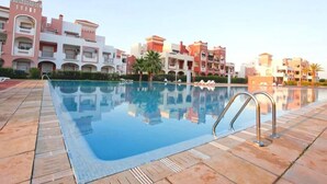 A swimming pool with a tiled edge and metal handrails, surrounded by multi-story buildings with balconies and a clear sky. - Residence Marina Saidia 4244 (Saidia)