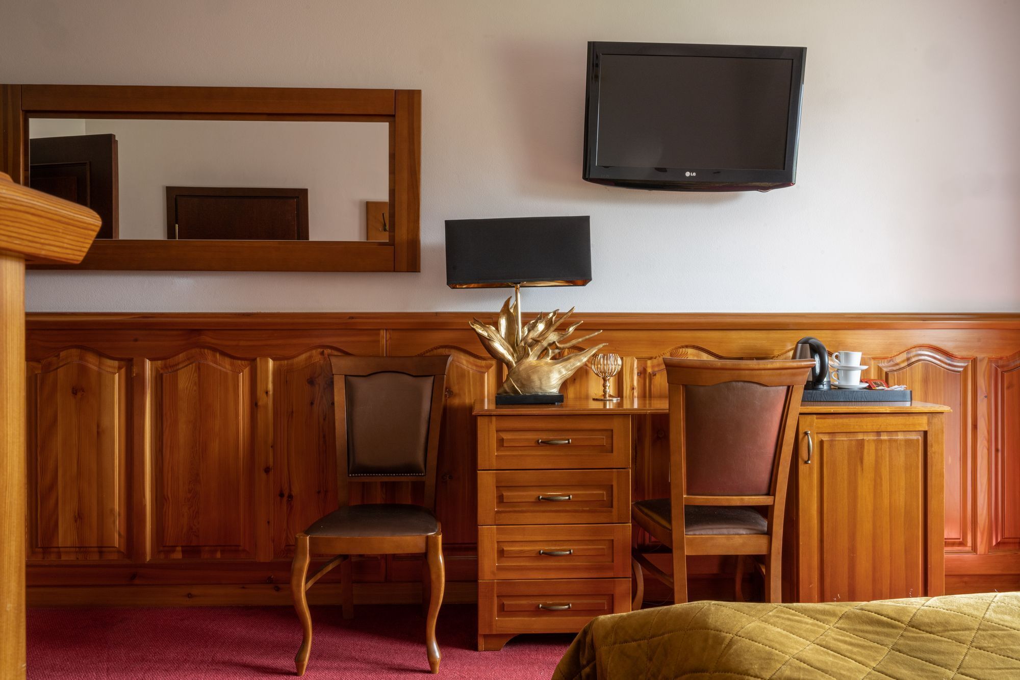 A hotel room with wooden furniture, a flat-screen TV, a desk with drawers, and a bed with a green quilt.