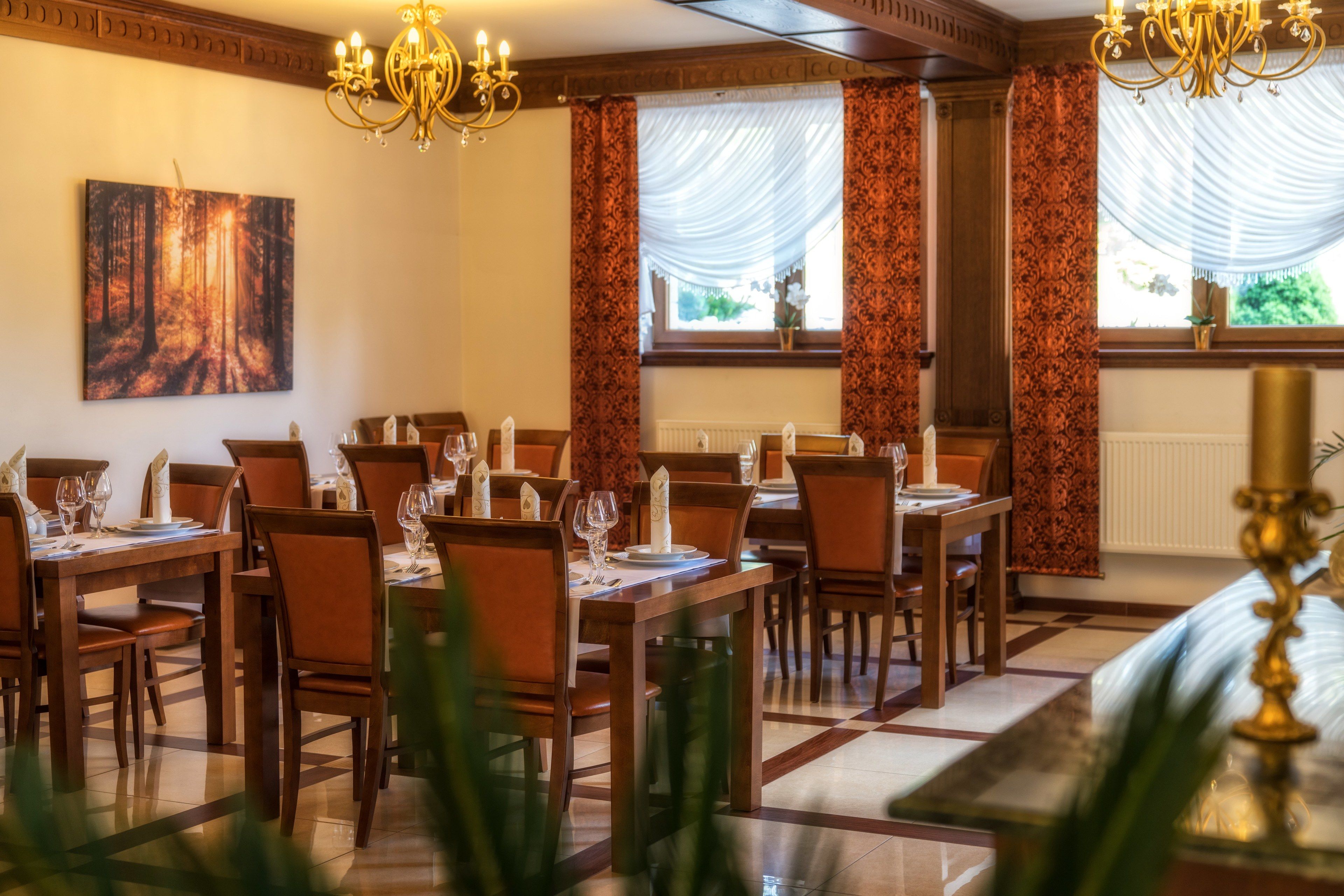 Un comedor con mesas y sillas de madera, candelabros y un cuadro en la pared.