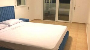 A bedroom with a bed, a nightstand, a window, and a sliding glass door leading to a balcony.