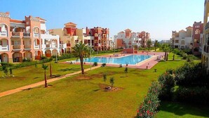 A hotel with a large swimming pool, multiple balconies, and a well-maintained garden.
