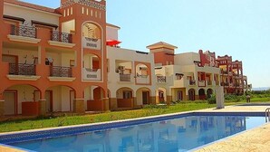 A hotel with multiple balconies, a swimming pool, and a garden area.