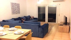 A living room with a blue sofa, a dining table set with plates and chopsticks, and a television on a stand.