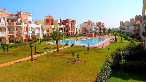 A hotel with a large swimming pool, multiple balconies, and a well-maintained garden. - Residence Marina Saidia 4239 (Saidia)