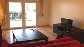 A living room with a red sofa, a black coffee table, a TV on a black stand, and a sliding glass door leading to an outdoor area. - Residence Marina Saidia 4239 (Saidia)