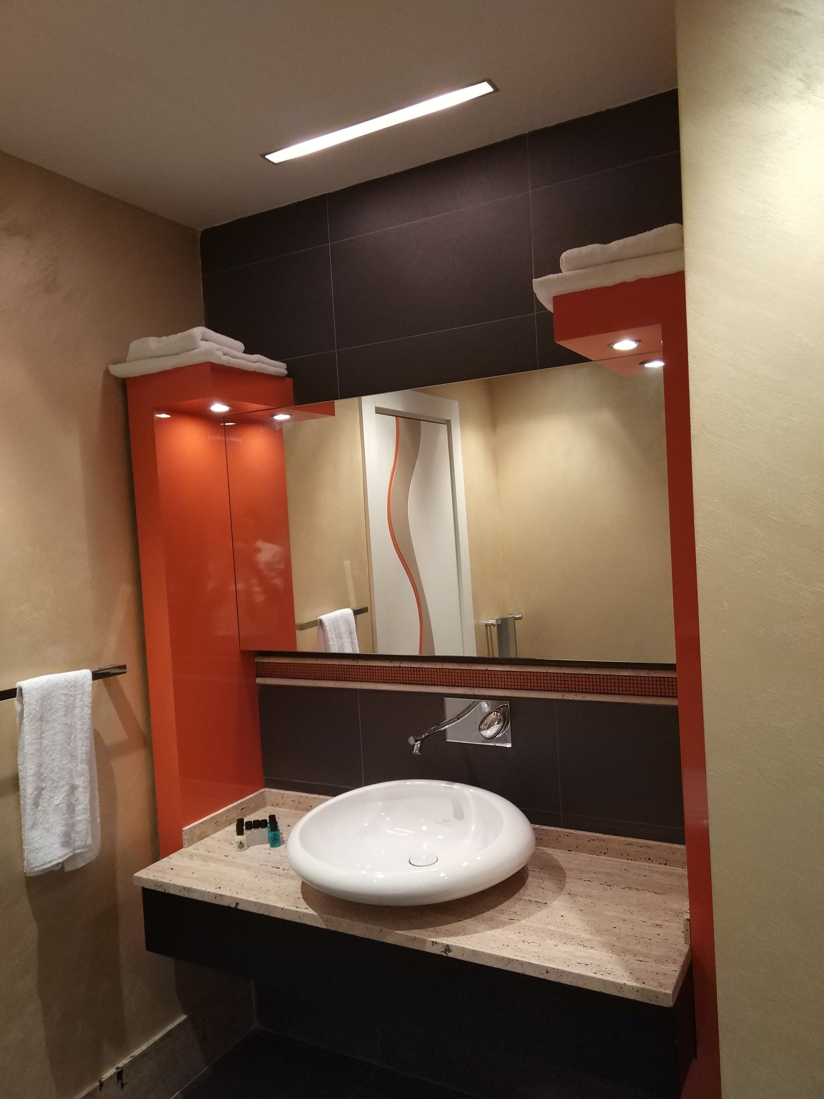 Un baño con un lavamanos blanco, un espejo y un perchero para toallas.