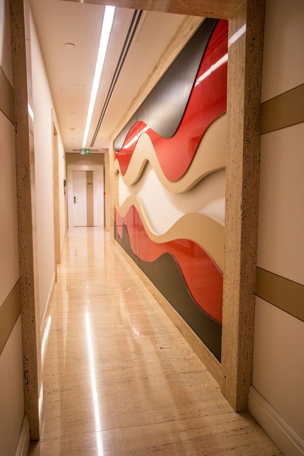 A modern hallway with a glossy marble floor, a red and white abstract wall art, and a door labeled "101" in the distance.
