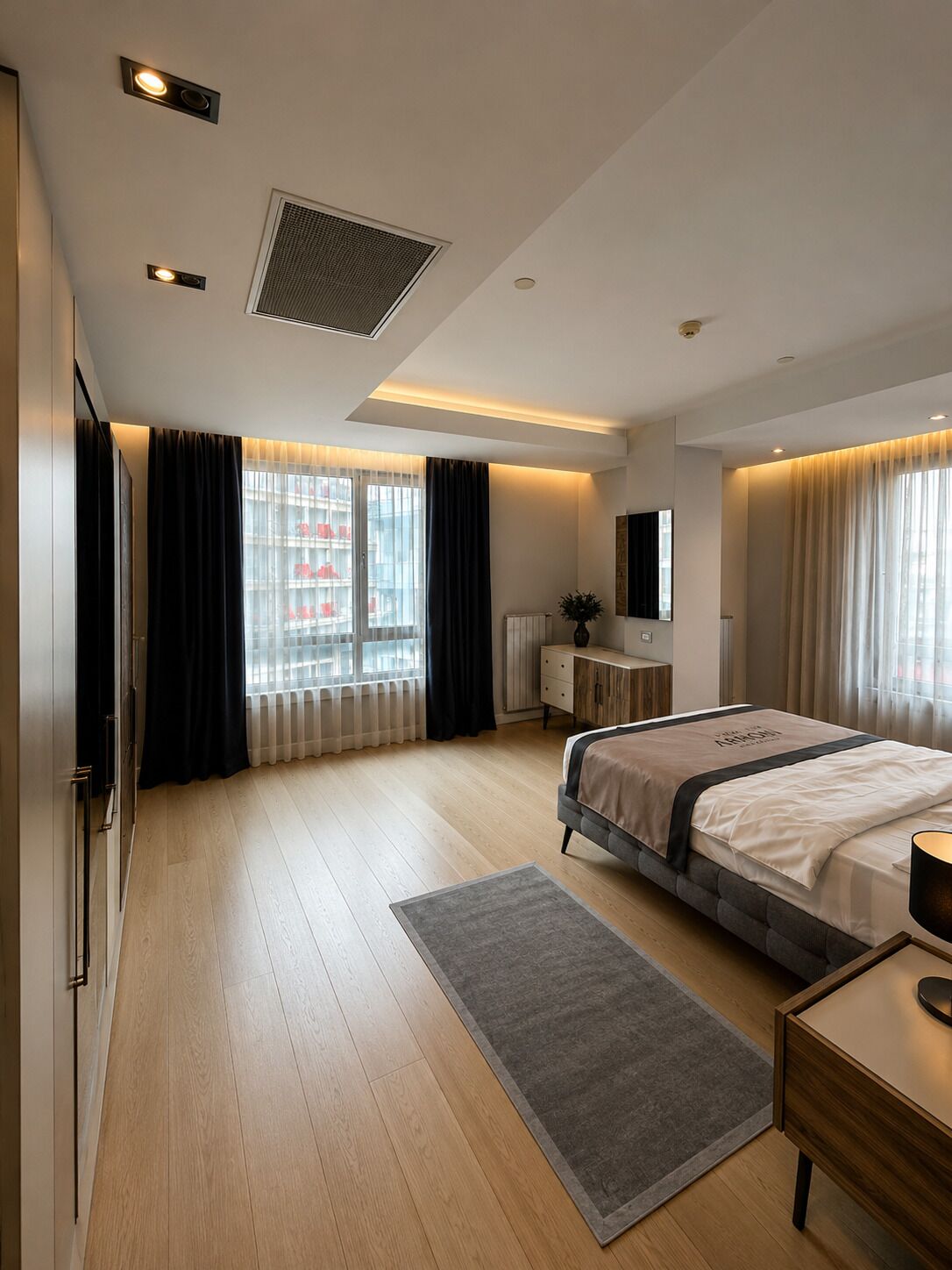 A modern hotel room with a large bed, a bedside table, a dresser, and a window with curtains.