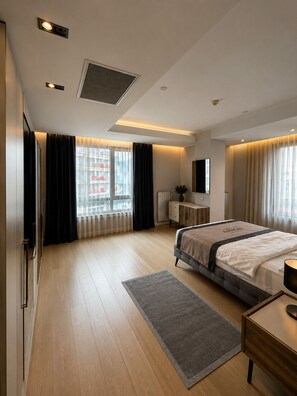 Quarto de hotel moderno com uma cama grande, mesa de cabeceira, cômoda e janela com cortinas.