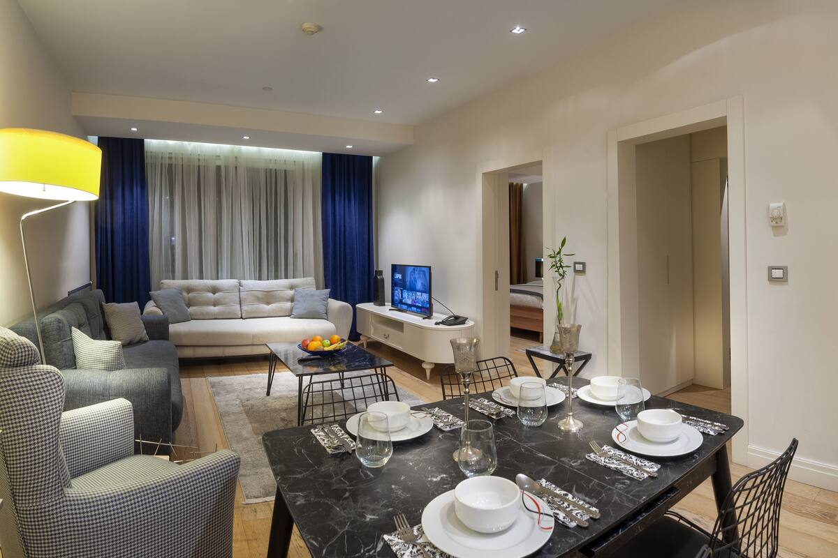 A modern living room with a sofa, dining table set for four, and a television.