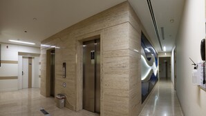 A modern hotel lobby with a marble reception desk, an elevator, and a long corridor with a decorative wall. - Armoni Residence (Istanbul)
