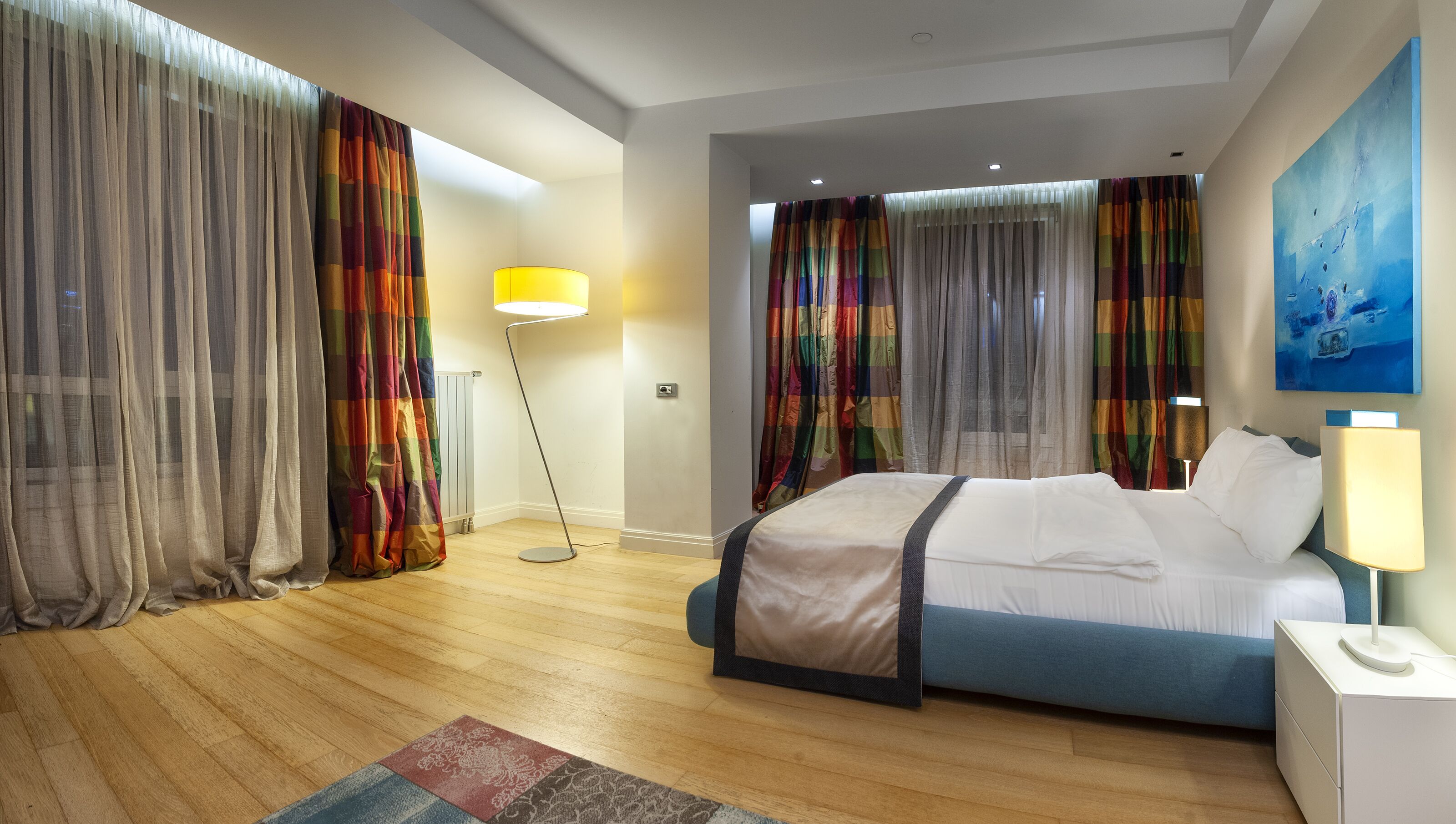 Una habitación de hotel moderna con una cama grande, una lámpara de pie y cortinas coloridas.