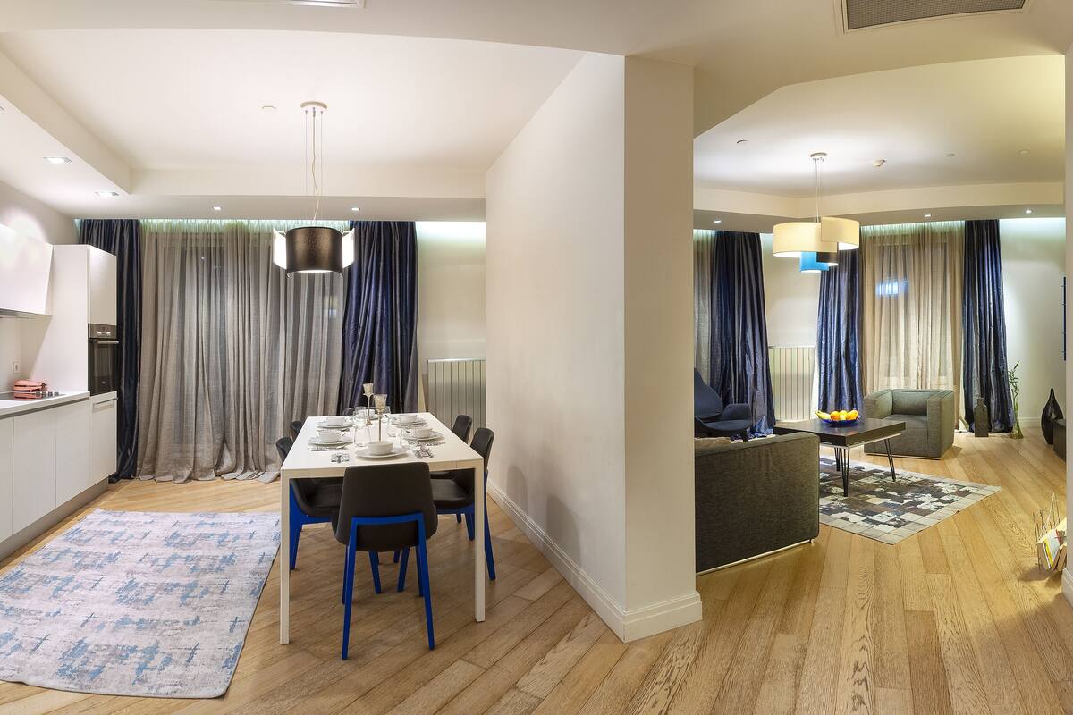 A modern kitchen with a dining area, wooden flooring, and a living space with a sofa and a coffee table.
