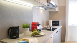 Cozinha moderna com micro-ondas, chaleira e cafeteira vermelha. Há uma pequena planta em vaso e um prato de legumes no balcão.