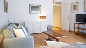 Uma sala de estar com um sofá, uma mesa de centro, uma TV sobre um suporte, um armário e um quadro na parede.