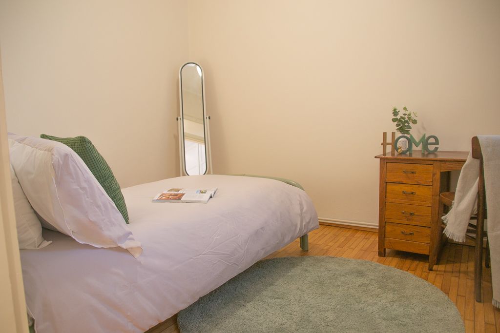 A bedroom with a bed, a mirror, a dresser, and a small plant.