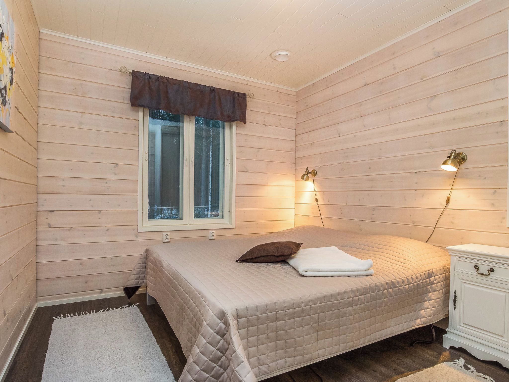 Ein Schlafzimmer mit einem Bett, einem Fenster, einem Nachttisch und einer Wandlampe.