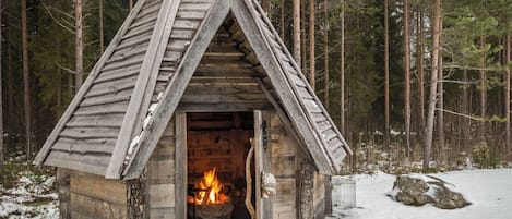 Una cabaña de madera con techo triangular, chimenea y terreno cubierto de nieve.