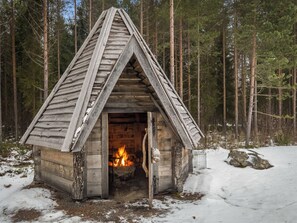 A wooden cabin with a triangular roof, a fireplace, and a snow-covered ground. - Kalaranta by Interhome (Pertunmaa)