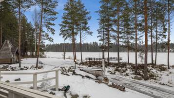 Lumipeitteinen maisema, jossa on puinen mökki, puinen terassi ja kirkas taivas.