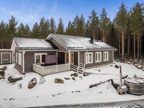 Une cabane à deux étages dotée d’un porche abrité, d’une cheminée et surplombant un paysage enneigé.