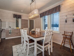 Un espace repas avec une table en bois, des chaises blanches et un luminaire suspendu.