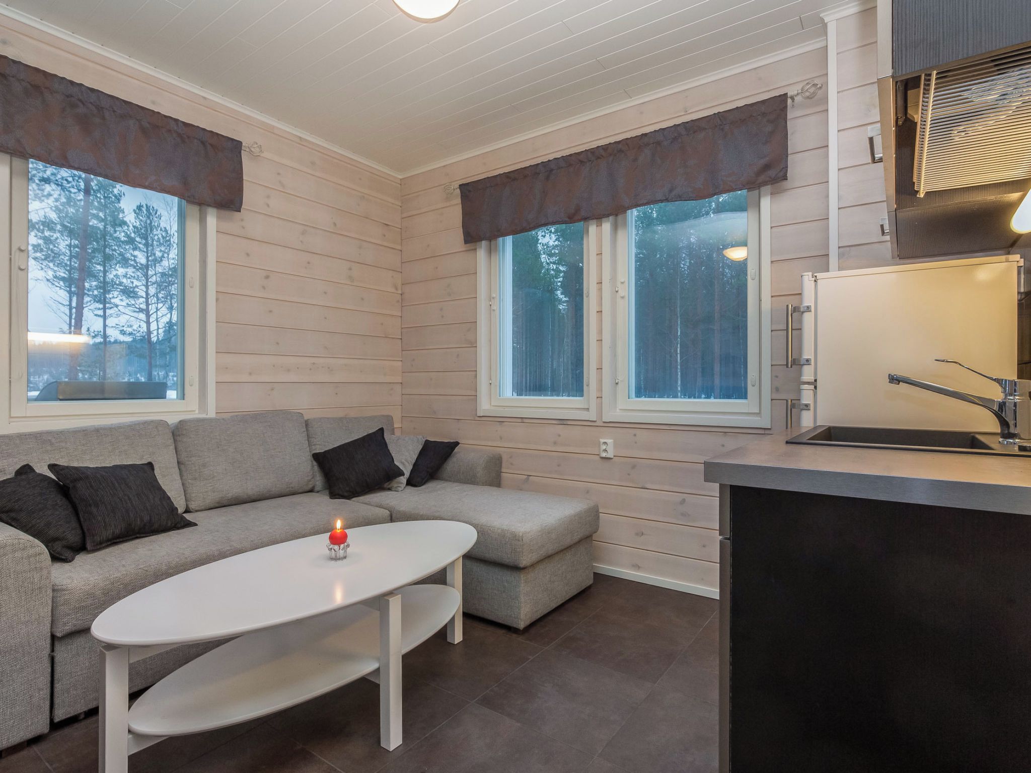 Ein modernes Interieur mit einem grauen Sofa, einem weißen Tisch und einer Küchenzeile mit eingebautem Herd.