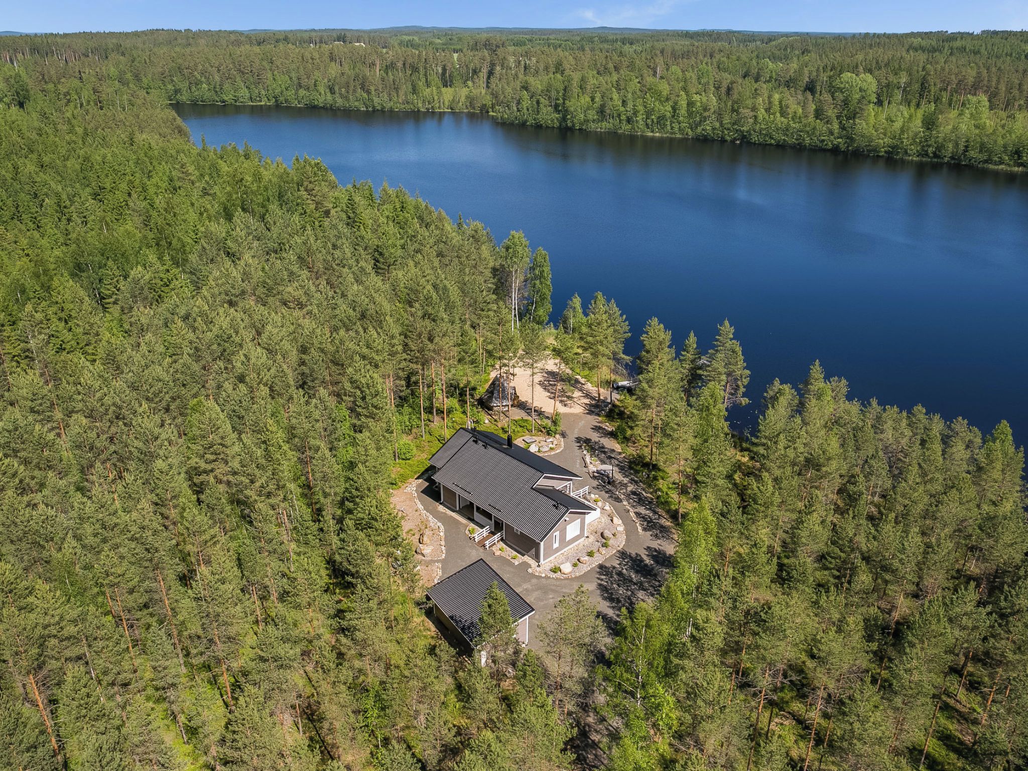 A lakeside property with a main building and a smaller structure, surrounded by dense forest.