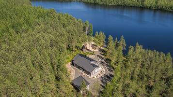 A lakeside property with a main building and a smaller structure, surrounded by dense forest.