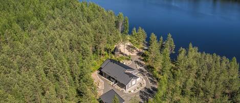 A lakeside property with a main building and a smaller structure, surrounded by dense forest.