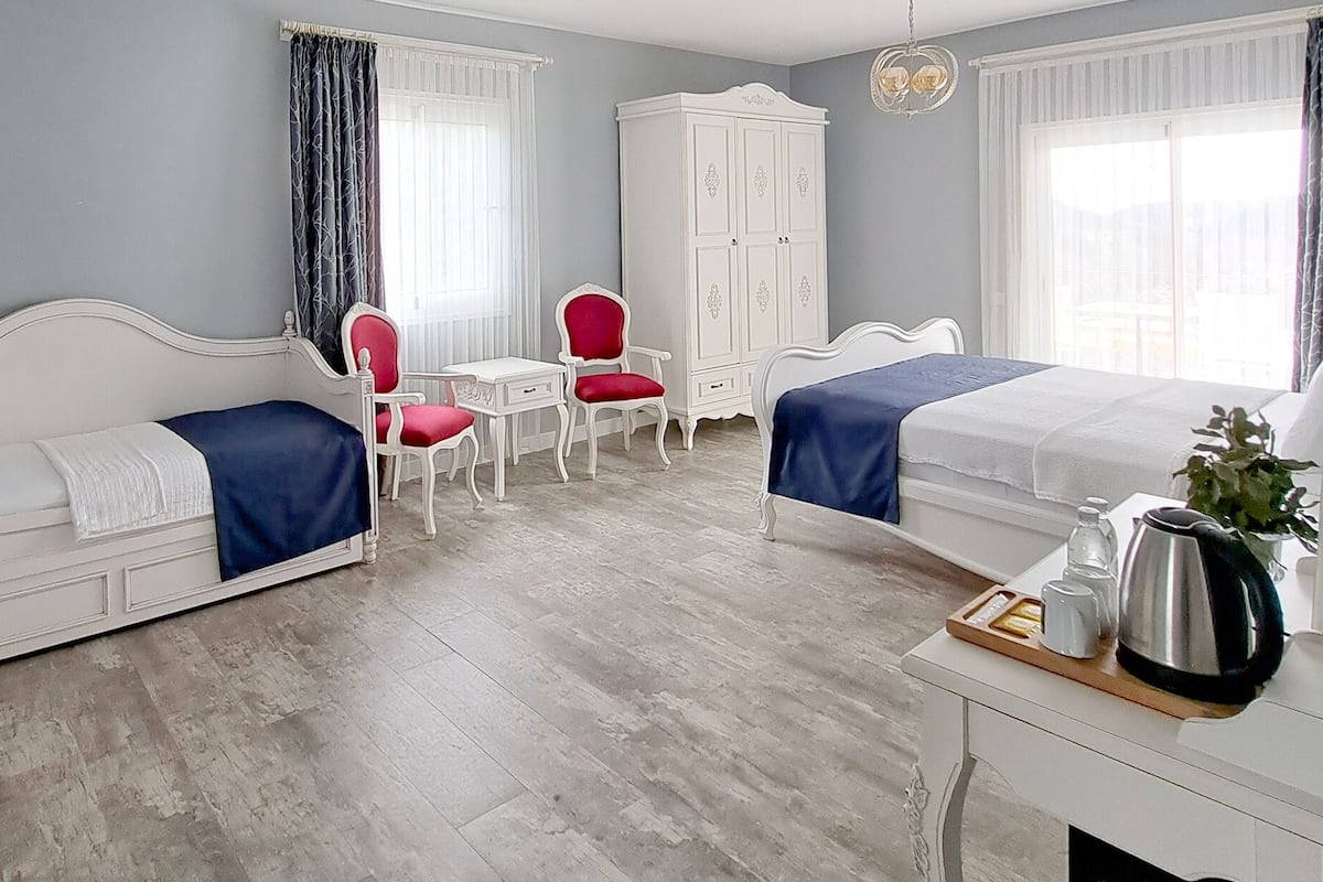 Ein Hotelzimmer mit zwei Betten, einem Schreibtisch, einem Stuhl, einem Kleiderschrank und einem Vorhangfenster.