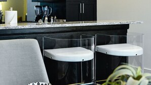 Una cocina moderna con gabinetes negros, un microondas de acero inoxidable y una encimera de mármol. Hay dos taburetes de bar y una mesa de comedor con cuencos decorativos.