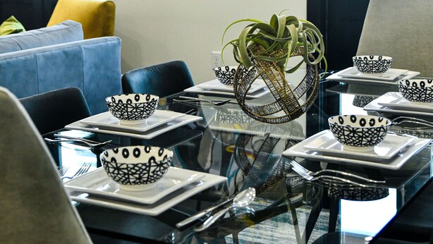 Un comedor moderno con una mesa de vidrio, sillas negras y platos blancos con diseños negros.