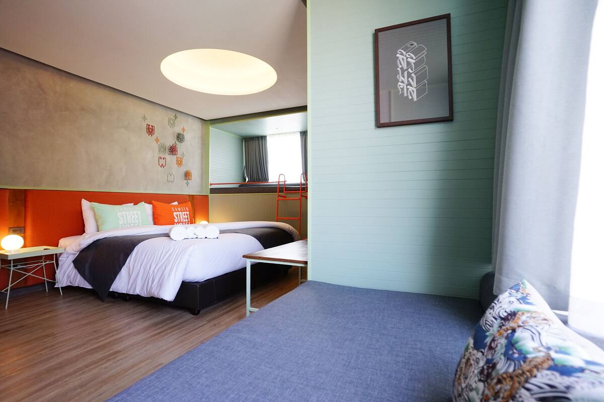 Een hotelkamer met een bed, bureau, stoel, bank, raam met gordijnen en een muur met een lijst erin.