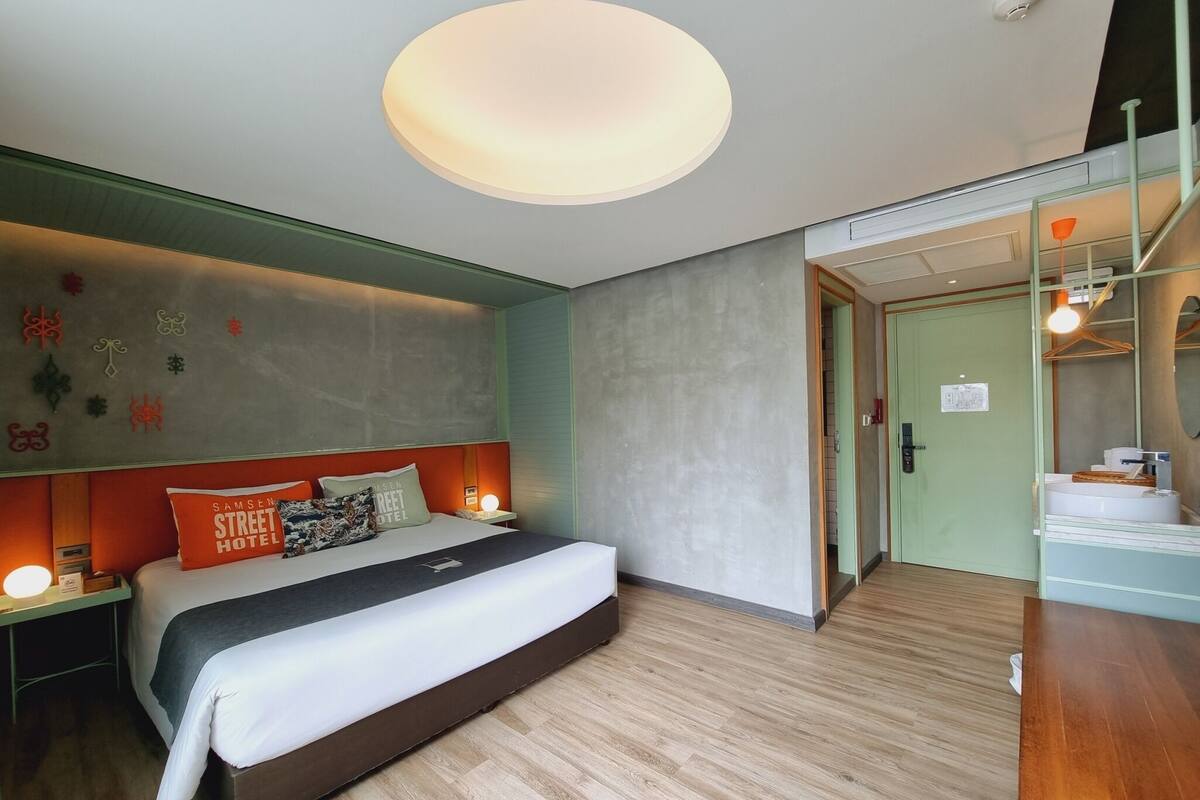 Een moderne hotelkamer met een groot bed, een nachtkastje, een wandlamp en een deur naar de badkamer.