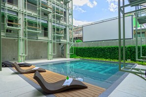 Zona de piscina con sillones de descanso y una gran pantalla blanca.